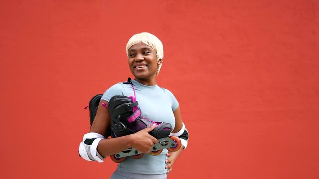 Portrait of african female skater with inline skates on shoulder standing outdoors next to red building