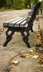 Color vertical photo, an old worn wooden bench with metal legs, on a bumpy asphalt road, on a sunny day.