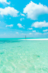 A man walks alone on a white sandy island with turquoise sea in the Maldives