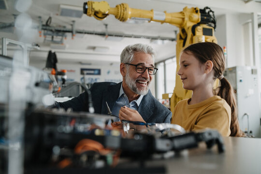 Father and girl during kid at work day, encouraging girl in career in robotics. Teacher showing young schoolgirl how to assemble small robot. - Powered by Adobe
