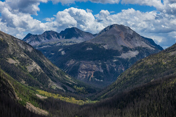 Obraz premium mountain forest valley with distant peaks and afternoon summer clouds
