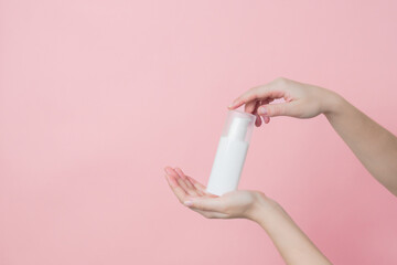White unbranded cream bottle with pump in hand on pink background. Concept of beauty. Product cosmetic advertising