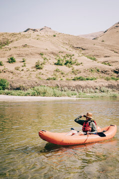 Man in Orange Kayak Navigates Serene River Amidst Rugged Hills