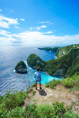 Man stands on a rock overlooking a beautiful bay with a turquoise beach at Nusa Penida, Bali, Indonesia. summer background and summer vacation concept. © Balnyes Visuals