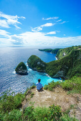 Man sit and watching beautiful scenery of hills beach island and blue ocean at Klingking Beach, Nusa Penida, Bali, Indonesia. summer background and summer vacation concept. © Balnyes Visuals