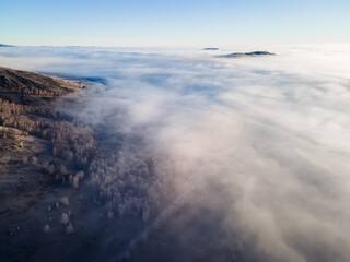 Clouds over the mountains and forest at foggy sunrise. Aerial view. Frost-covered trees in a forest.