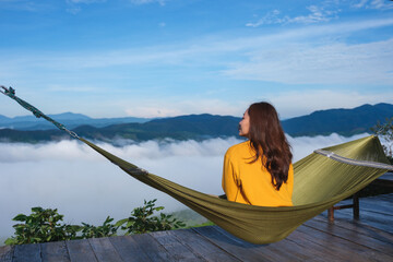 Rear view of a woman sitting on hammock and looking at a mountain view and sea of fog