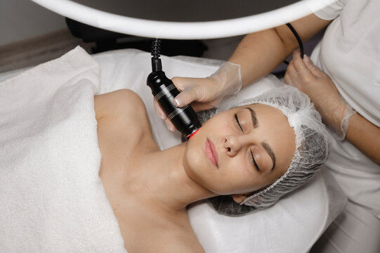 Young dermatologist doing Rf lifting procedure on woman's face