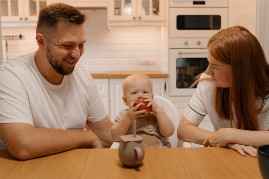 Parents looking at son eating apple in home