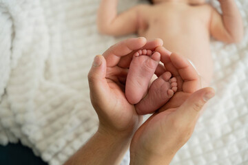Father holding feet of new born baby lying on bed