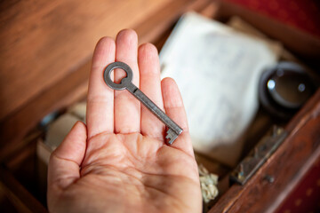 A woman holds an old key in her hand next to an old wooden box containing family memories.