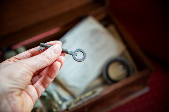 A woman holds an old key in her hand beside an old wooden box filled with family memories.
