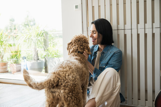 Smiling woman playing with dog at home