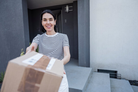 Smiling woman receiving parcel box from delivery person in front of house