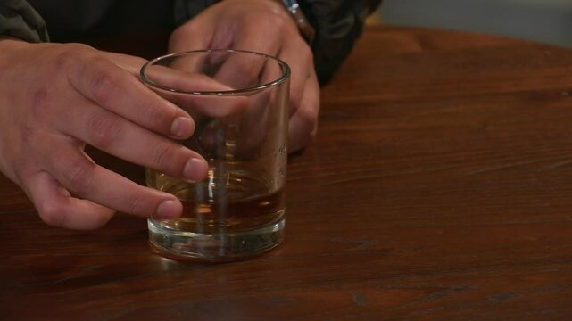 Male hands turning and swirling what looks like an alcoholic drink in a glass.  Concept for alcohol abuse.  
