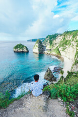 Back view man on the edge of a cliff looking at Diamond Beach, Nusa Penida, Bali, Indonesia. summer background and summer vacation concept. © Balnyes Visuals