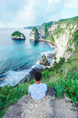 A young traveler looks at the amazing views from the top of the cliff at Diamond Beach, Nusa Penida, Bali, Indonesia. summer background and summer vacation concept.  © Balnyes Visuals