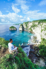 Young man sitting on the cliff and enjoying the view at Diamond Beach, Nusa Penida, Bali, Indonesia. summer background and summer vacation concept. © Balnyes Visuals