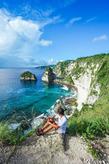 Young traveller sitting and relaxing on top of t Diamond Beach, Nusa Penida, Bali, Indonesia. summer background and summer vacation concept.  © Balnyes Visuals
