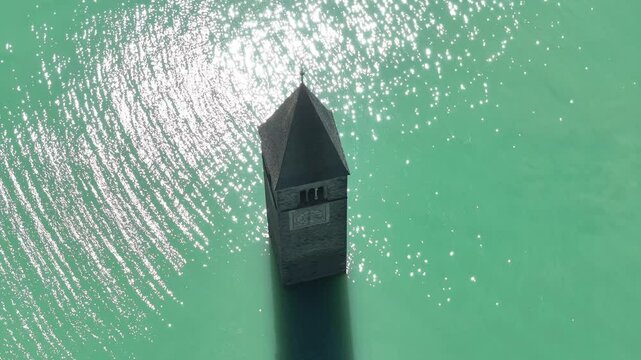 An aerial view of the submerged bell tower of Curon Venosta emerging from Lake Reschen in South Tyrol, Italy, providing a rare glimpse into the region's historical and natural beauty.