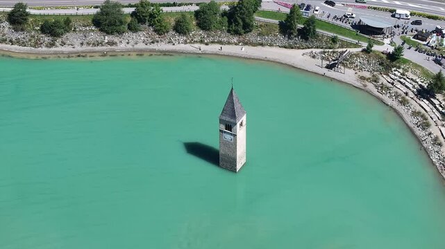 An aerial perspective of the submerged bell tower of Curon Venosta (Graun im Vinschgau) emerging from Lake Reschen in South Tyrol, Italy, view into the area's historical and natural splendor.