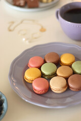 Plate of pastel macarons, cookies and chocolate, cup of tea of coffee, glass of bubble water, various berries, books and accessories on the table. Selective focus, pastel colors.