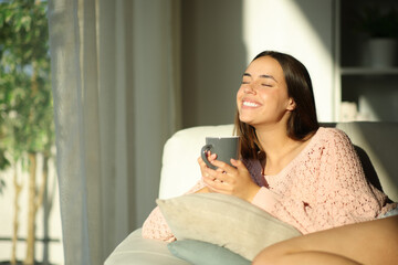 Happy woman breathing drinking coffee at sunset at home