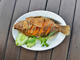 ikan nila or fried fish tilapia is served on a white plate. a type of freshwater fish cultivated in ponds