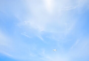 Fototapeta premium Airplane flying high in a clear blue sky with fluffy white clouds.