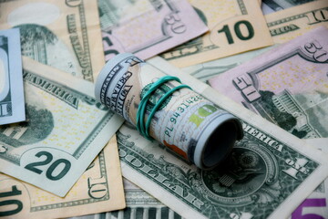 Hundred dollar bills roll lies on big amount of US dollars in different nominations under natural light