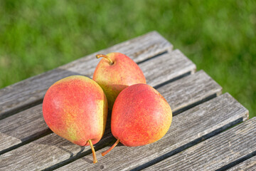 Three pears on a wooden table on a green lawn background