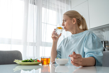 A woman is having a salad and tea in her modern kitchen, filled with sunlight and a serene ambiance