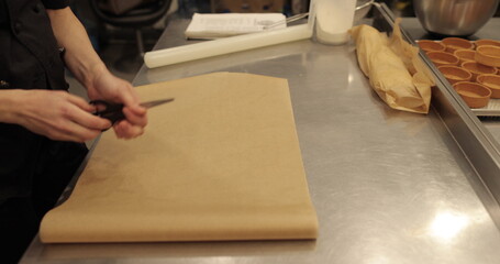 A cook prepares dough for cakes on a large, professional, metal table.