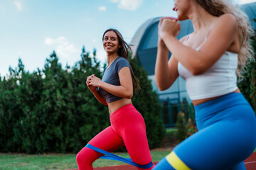 Two sporty girls exercising on a track, wearing sporty outfits. They are using resistance bands while training, showcasing a dynamic workout session.