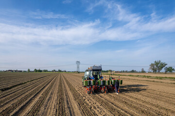 Fototapeta premium Farmers working with automatic tomato planter machine in a field, planting crops and laying down irrigation pipes