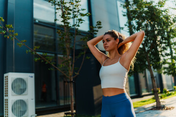 Jogging outdoors, a young woman ties her hair into a ponytail, dressed in a gray crop top and red leggings. Modern buildings and trees surround her.