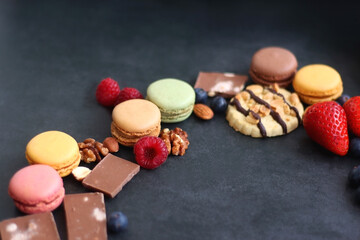 Macarons, chocolate, cookies, berries and various nuts on dark blue background. Selective focus.