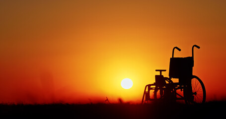 A wheelchair silhouetted against a vivid sunset, with a bright orange sky.