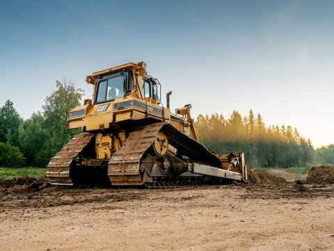 Ogre area, Latvia - 07.15.2024: Massive powerful CAT bulldozer in rural forest area. Construction and development job. Heavy machinery at work. Sunrise time. Nobody.