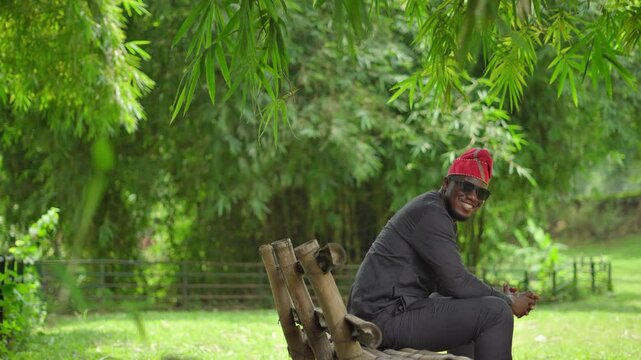 Nigerian Yoruba male sitting in garden turns to face the camera and nods and smiles.
