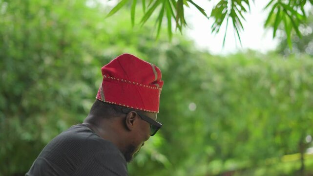 African-American male in Yoruba cultural hat talking excitedly in a garden.
