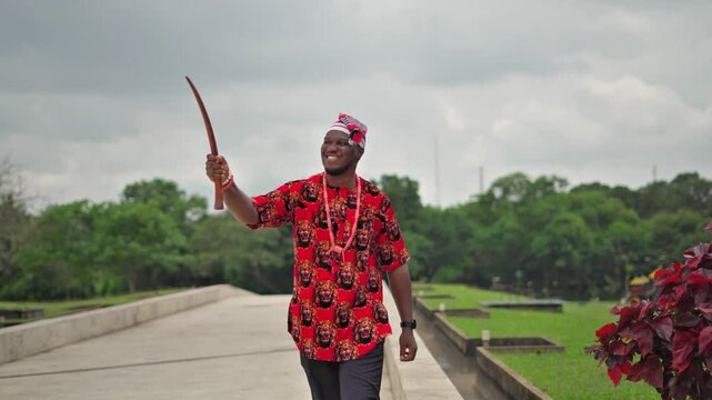 Igbo titled man greeting imaginary people smiling and walking with his mantle in his hand.
