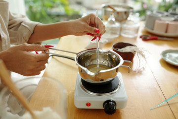 Close-up of woman melting wax in bowl for candles while sitting at table in the room
