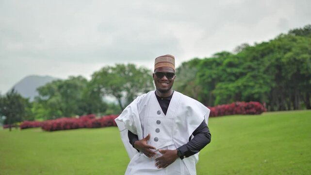 Young African male adjust his Babariga dress as he walks towards the camera while outdoor in Nigeria