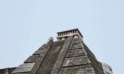 Gray rock stone pyramid styled building structure exterior isolated on horizontal ratio plain sky background.