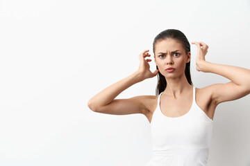 frustrated woman with long dark hair in white tank top, touching her hair, expressing confusion or annoyance against a plain white background