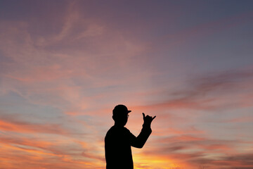 silhouette of a man in sunset making a shaka sign