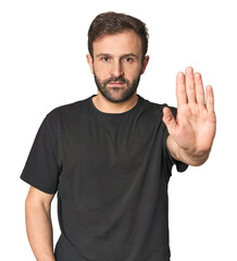 Naklejka premium Studio portrait of young Hispanic male standing with outstretched hand showing stop sign, preventing you.