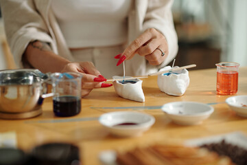 Close-up of woman putting wick in wax while making handmade candles at table