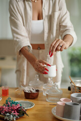 Woman putting wick in wax to make handmade candles during her leisure time at home